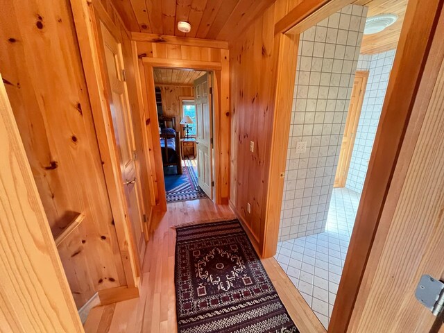 corridor featuring tile walls, wooden walls, wood ceiling, and light hardwood / wood-style floors