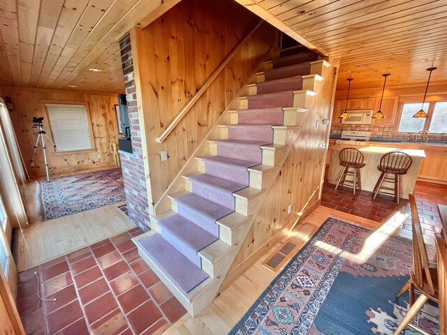 staircase with wooden ceiling, wooden walls, sink, hardwood / wood-style floors, and brick wall