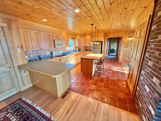 kitchen featuring light brown cabinetry, white appliances, a breakfast bar, wood-type flooring, and kitchen peninsula