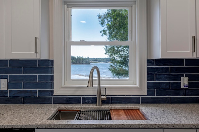 kitchen with light stone countertops, sink, tasteful backsplash, white cabinetry, and a water view