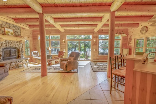living area featuring beam ceiling, light wood-style flooring, wood ceiling, wooden walls, and a stone fireplace