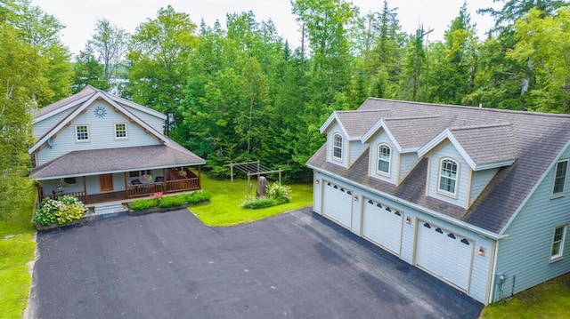 exterior space with covered porch, a garage, driveway, roof with shingles, and a front yard