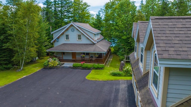 view of front of property with covered porch, a shingled roof, and a front lawn