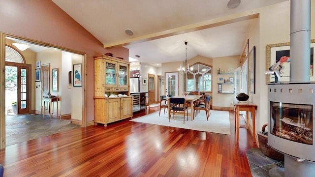 dining space featuring lofted ceiling with beams, a notable chandelier, dark wood-type flooring, and a glass covered fireplace