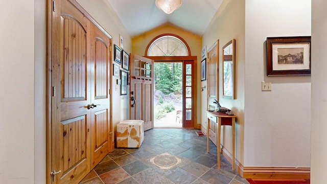 entrance foyer featuring lofted ceiling, stone tile flooring, and baseboards