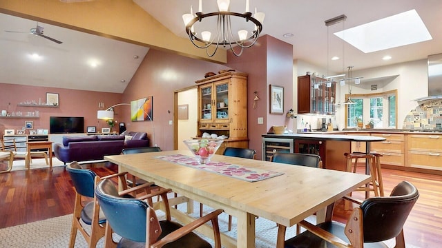 dining space with recessed lighting, beverage cooler, ceiling fan with notable chandelier, light wood finished floors, and lofted ceiling with skylight