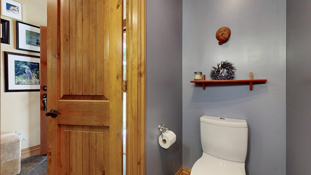 bathroom featuring stone finish floor, toilet, and baseboards