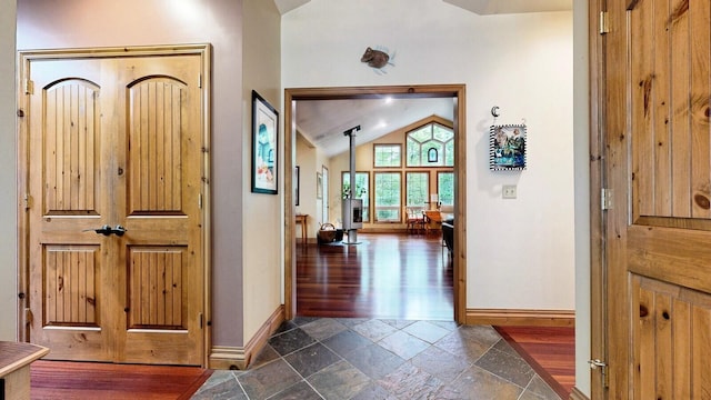 foyer entrance with high vaulted ceiling, a wood stove, baseboards, and stone tile floors