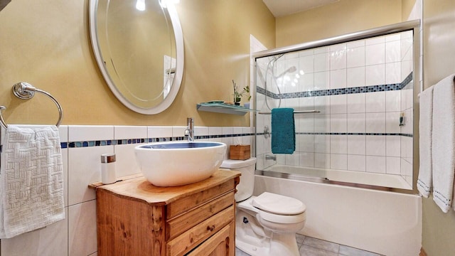 full bathroom with toilet, shower / bath combination with glass door, tile patterned floors, vanity, and tile walls