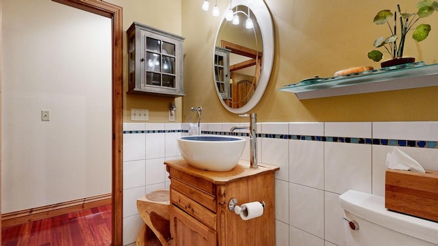 half bath with a wainscoted wall, tile walls, toilet, vanity, and wood finished floors