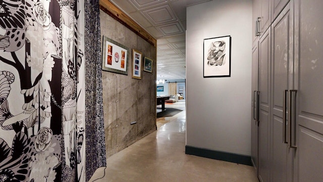 corridor with finished concrete flooring, an ornate ceiling, and baseboards