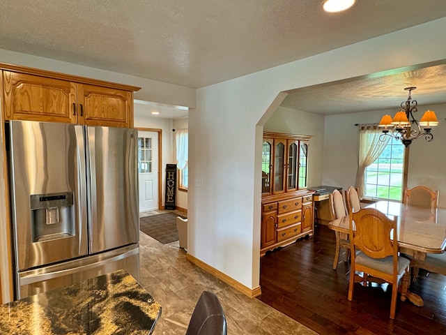 kitchen featuring a textured ceiling, baseboards, stainless steel fridge with ice dispenser, brown cabinetry, and an inviting chandelier