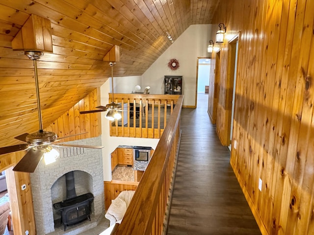 hall featuring dark wood-type flooring, wood ceiling, vaulted ceiling, wooden walls, and an upstairs landing