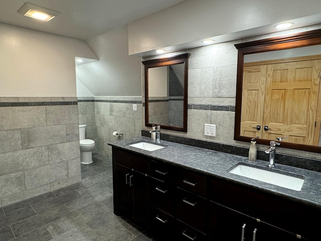 bathroom featuring toilet, double vanity, a sink, and tile walls