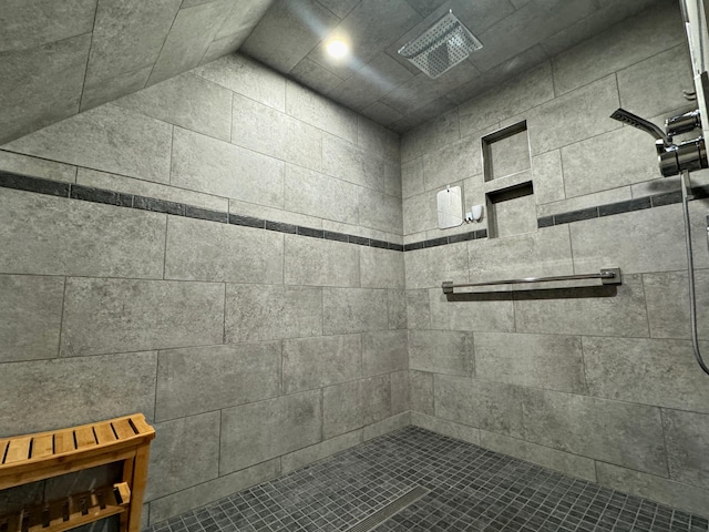 bathroom with lofted ceiling, tiled shower, and visible vents