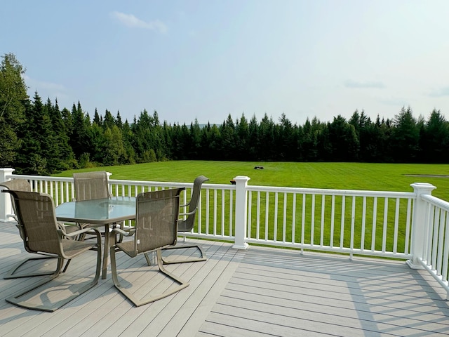 wooden terrace with outdoor dining area, a wooded view, and a yard