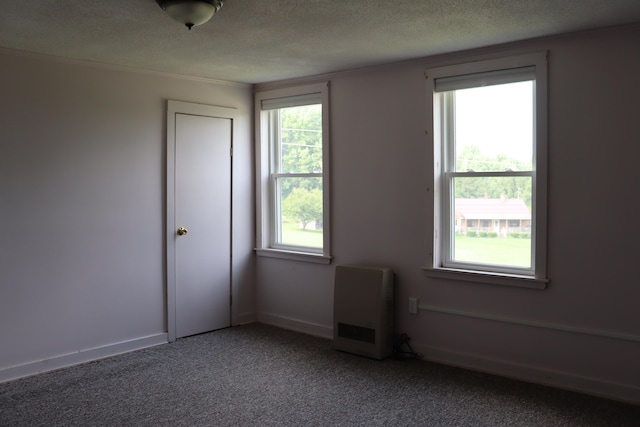 carpeted spare room featuring heating unit and a textured ceiling