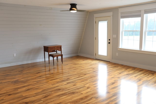 interior space featuring ceiling fan, wood walls, light hardwood / wood-style floors, and a healthy amount of sunlight