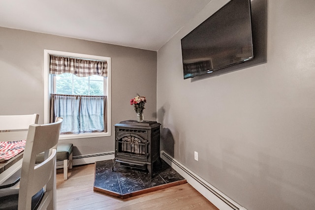 sitting room featuring light hardwood / wood-style floors, a wood stove, and a baseboard radiator