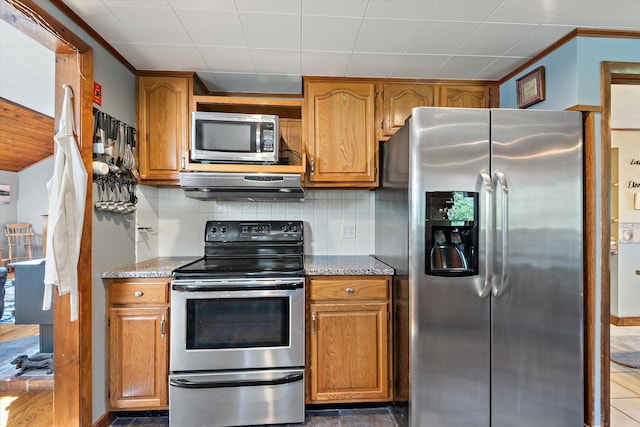 kitchen featuring brown cabinets, under cabinet range hood, appliances with stainless steel finishes, and decorative backsplash