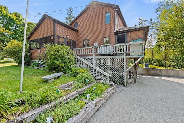 rear view of property featuring a lawn, stairway, a sunroom, a deck, and a garden