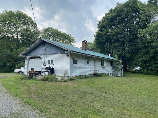 view of property exterior with metal roof, a garage, a chimney, and a yard