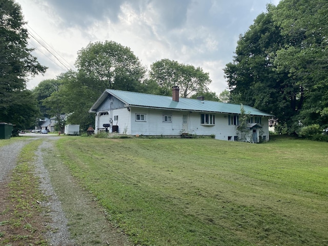 rear view of property with driveway, a yard, an attached garage, metal roof, and a chimney