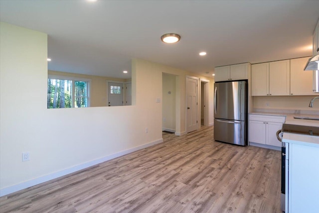 kitchen with sink, light hardwood / wood-style flooring, white cabinets, and stainless steel refrigerator