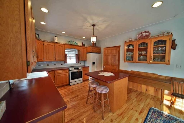 kitchen featuring stainless steel electric range, white refrigerator with ice dispenser, a breakfast bar, a center island, and light wood-type flooring