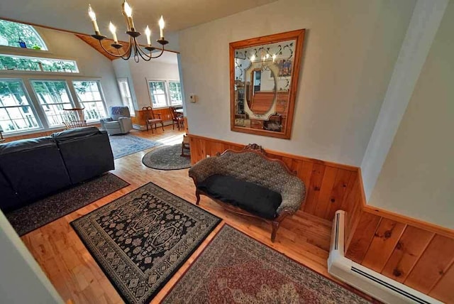 living room with an inviting chandelier, vaulted ceiling, wood walls, light hardwood / wood-style floors, and a baseboard radiator