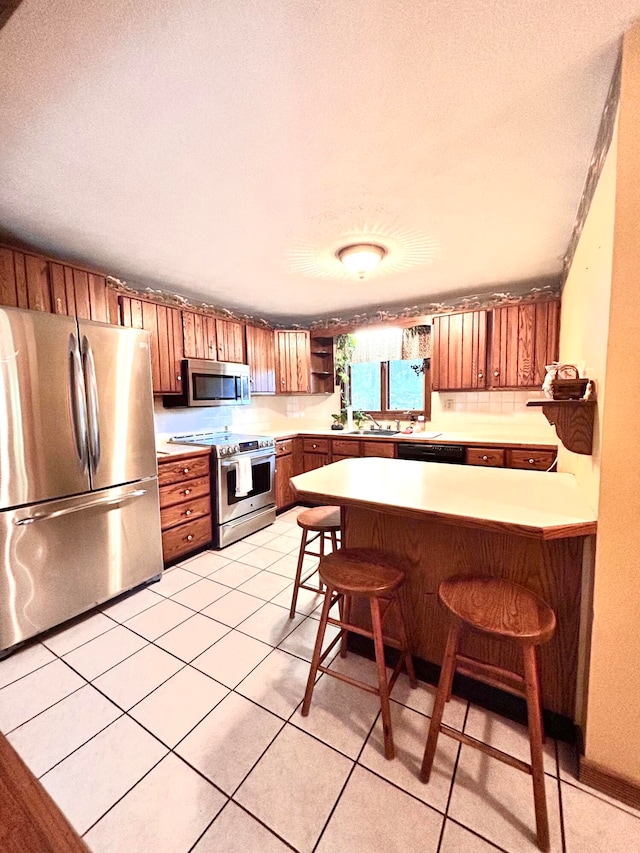 kitchen featuring a textured ceiling, a kitchen bar, stainless steel appliances, kitchen peninsula, and light tile patterned flooring