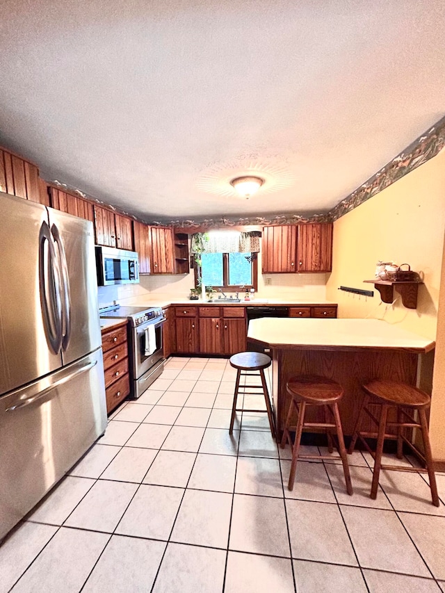 kitchen with a textured ceiling, light tile patterned floors, a breakfast bar, stainless steel appliances, and kitchen peninsula