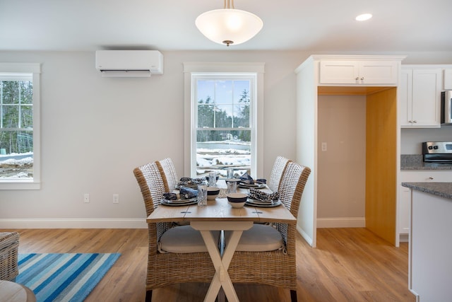 dining space featuring light wood finished floors, plenty of natural light, baseboards, and a wall mounted air conditioner