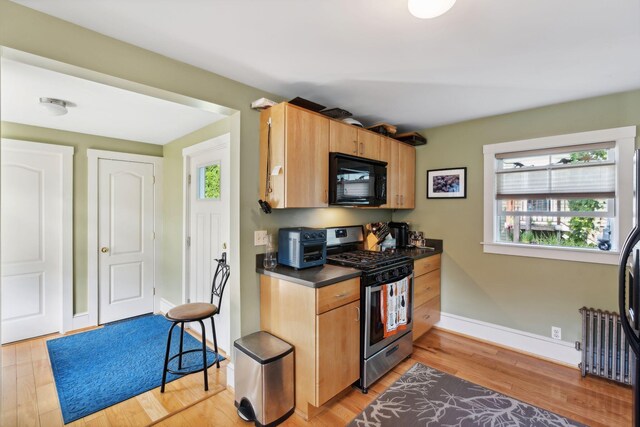 kitchen with light hardwood / wood-style flooring, stainless steel gas range, radiator, and a healthy amount of sunlight