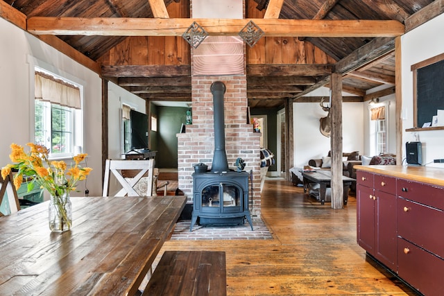 dining space with lofted ceiling with beams, hardwood / wood-style flooring, a wood stove, and wood ceiling