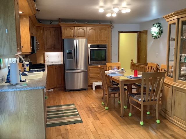 kitchen featuring appliances with stainless steel finishes, light hardwood / wood-style flooring, light stone counters, and a notable chandelier