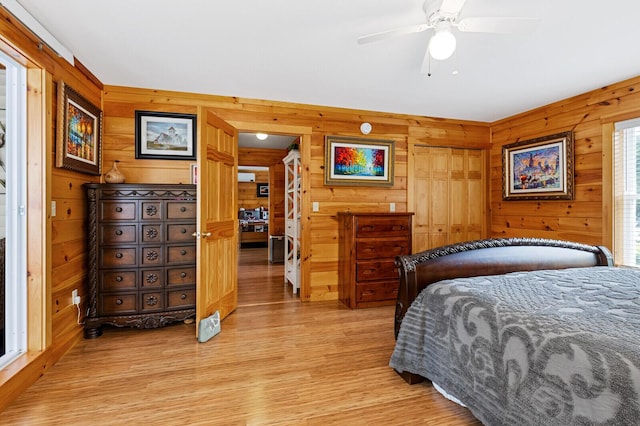 bedroom with ceiling fan, wooden walls, and light wood-style floors