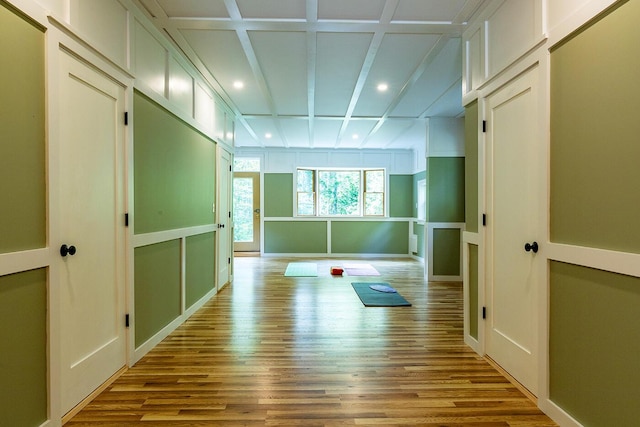 exercise area with light wood-type flooring, coffered ceiling, and a decorative wall