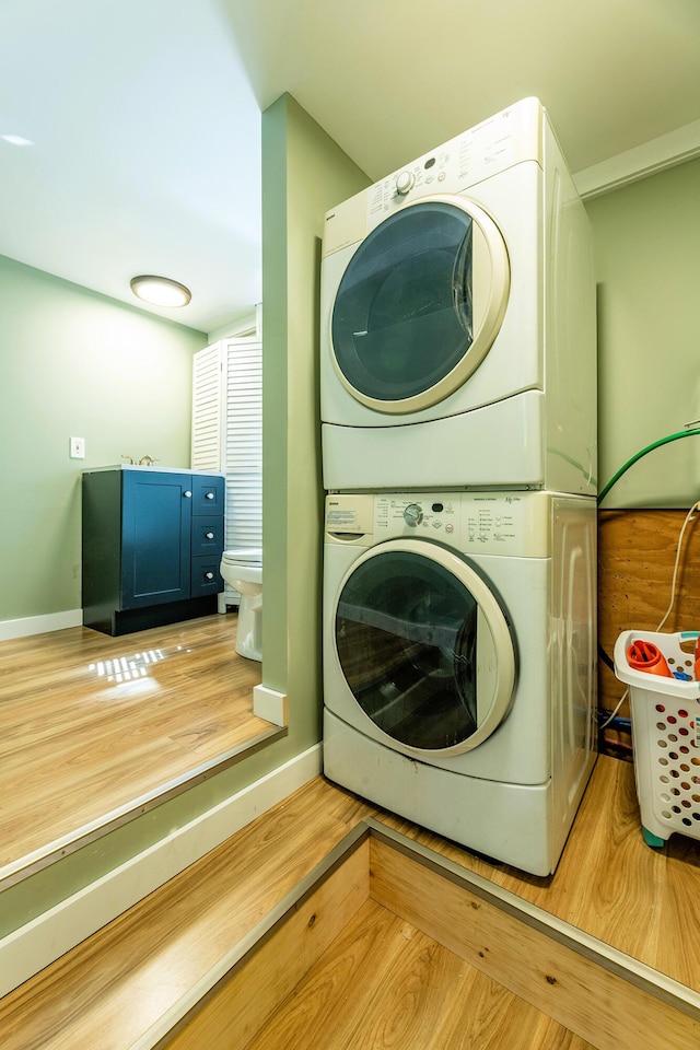 laundry area featuring laundry area, stacked washing maching and dryer, wood finished floors, and baseboards