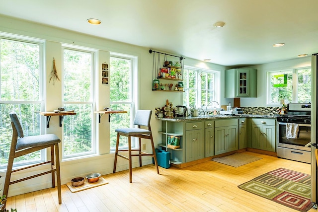 kitchen with light wood-style flooring, stainless steel range with gas cooktop, glass insert cabinets, and open shelves