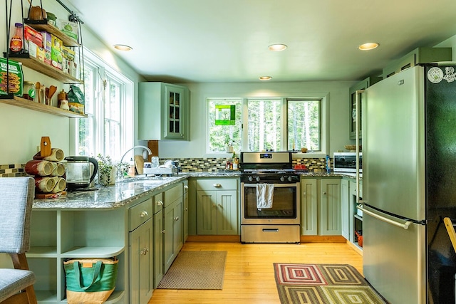 kitchen featuring stone countertops, a sink, appliances with stainless steel finishes, decorative backsplash, and glass insert cabinets