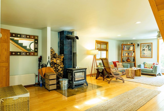 sitting room featuring recessed lighting, wood finished floors, baseboards, radiator heating unit, and a wood stove