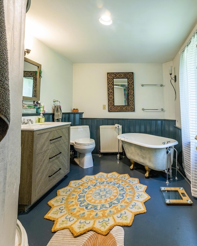 bathroom with toilet, radiator heating unit, concrete floors, and wainscoting