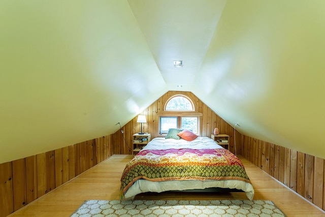 bedroom with light wood-style floors, vaulted ceiling, and wood walls