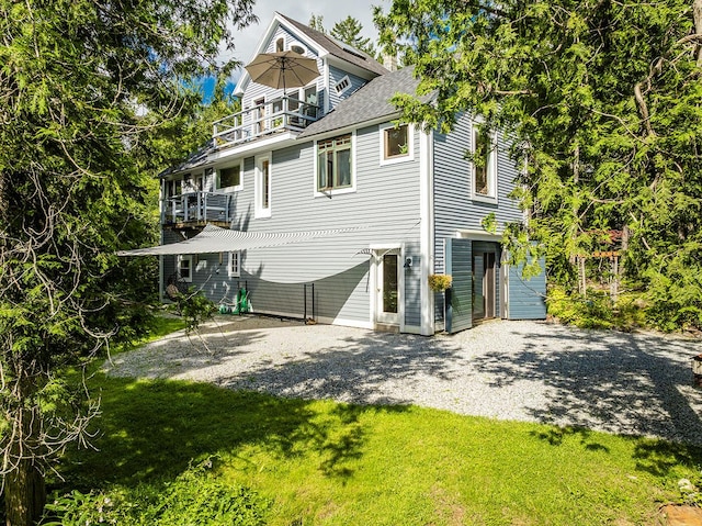 back of property featuring a balcony, driveway, and a yard