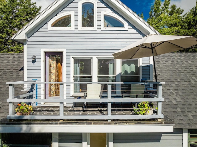 rear view of house featuring a shingled roof and a balcony