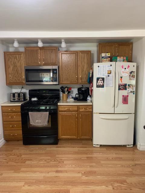 kitchen featuring beam ceiling, white fridge, light wood-type flooring, and black range with gas cooktop