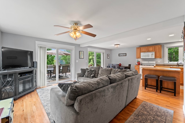 living room with light wood-type flooring, ceiling fan, beam ceiling, and sink