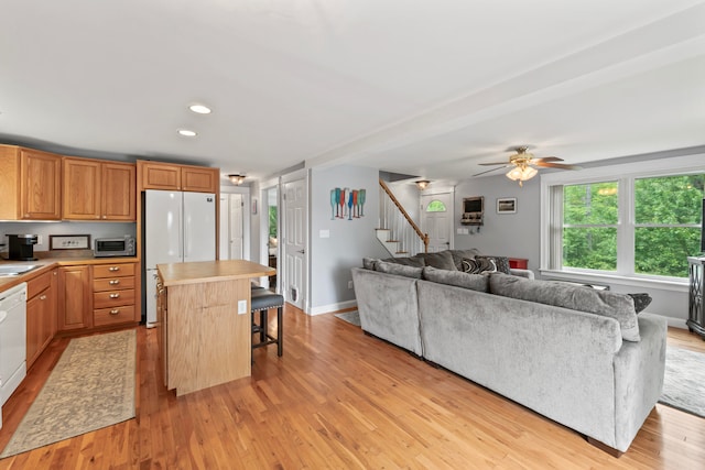 kitchen with light wood-type flooring, white appliances, a center island, ceiling fan, and a breakfast bar area