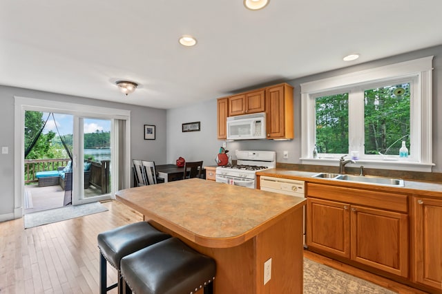 kitchen featuring white appliances, light hardwood / wood-style flooring, a kitchen breakfast bar, a kitchen island, and sink